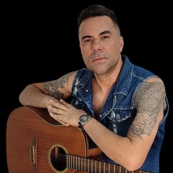 Luciano Lins de colete jeans, apoiado no violão